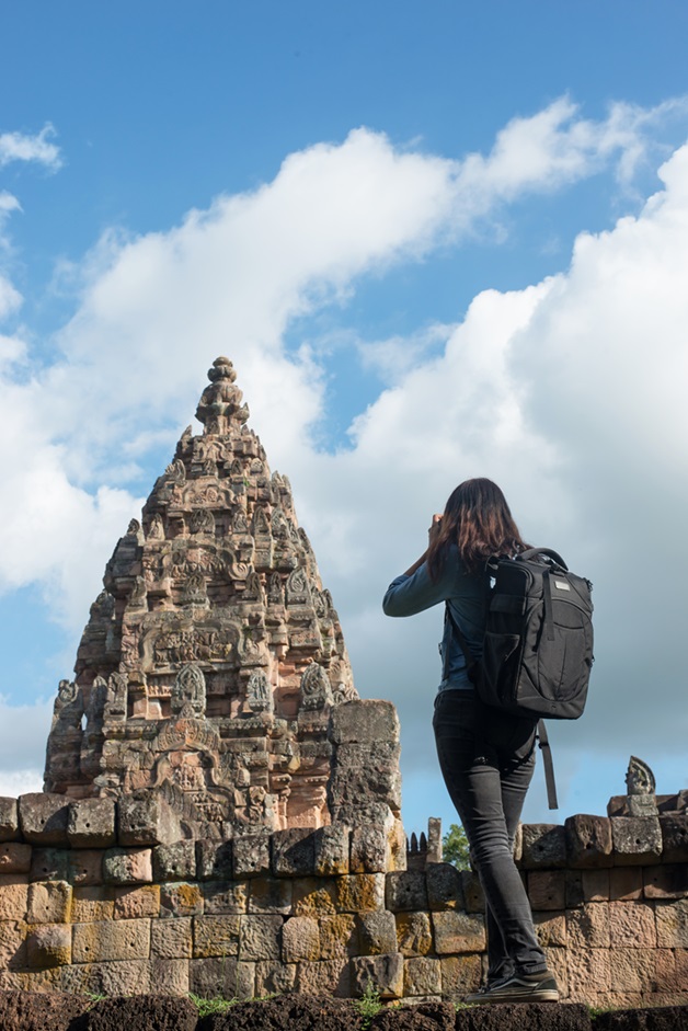 Young attractive woman photographer tourist with backpack coming to shoot photo at ancient phanom rung temple in thailand.