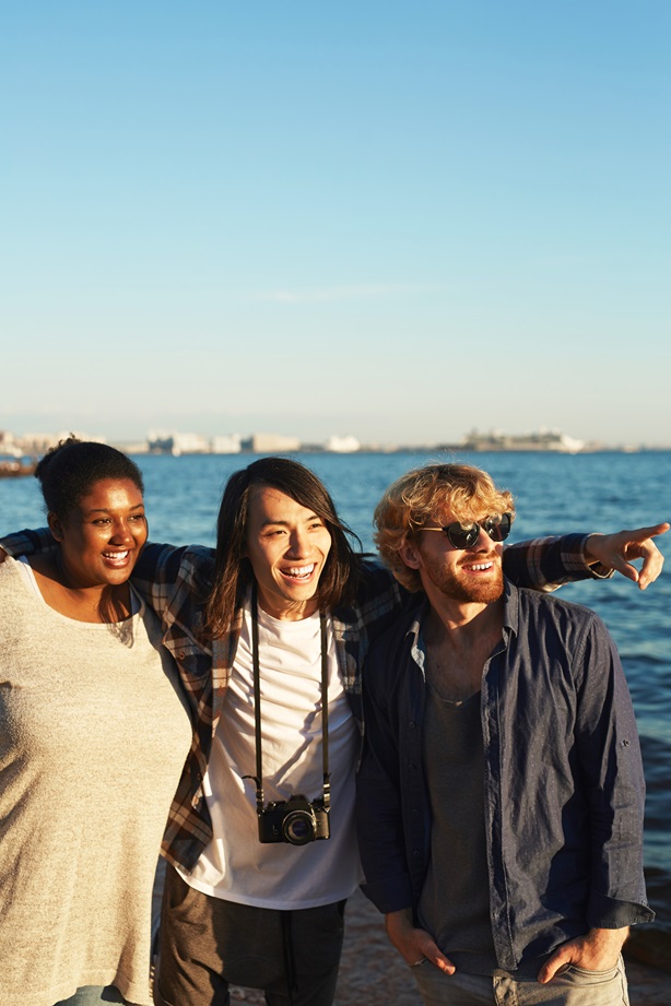 Three young friends looking straight where one of them pointing while enjoying summer day by seaside