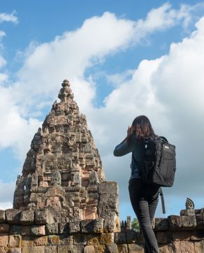 Young attractive woman photographer tourist with backpack coming to shoot photo at ancient phanom rung temple in thailand.